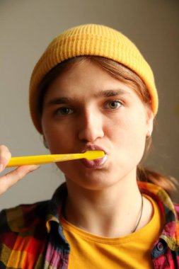 Sarı şapkalı genç bir hippi kadın, yakın planda dişlerini fırçalıyor. Onun tuhaf ifadesi ve modern görünüşü anı hem taze hem de stil sahibi yapıyor..