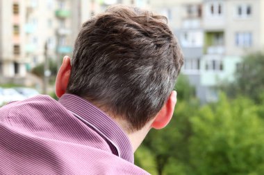 Genç bir adamın ensesinde, temiz bir arkaplan üzerinde gri saçlar görünüyor. Fotoğraf, erken grileşme kavramını vurguluyor ve ya kabul etme ya da boyama kararını veriyor..