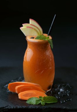 Cam kavanozda havuç suyu ve tahta bir masada meyve parçaları, seçici bir odak noktası.