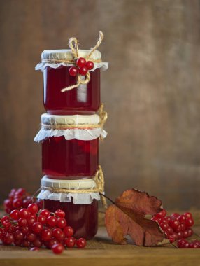 Viburnum fruit jam in a glass jar on a wooden table near the ripe red viburnum berries. Source of natural vitamins.