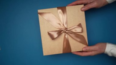 Craft paper gift box with a bow on a blue table. Flat lay composition for birthday, mothers day, black friday sale, christmas, xmas, new year