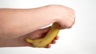 Stüdyo fotoğrafında kadın eli muz tutuyor, soyuyordu ve ısırmak üzereydi. Sağlıklı meyvelerle birlikte kahvaltıyı bembeyaz yapıyorlardı.