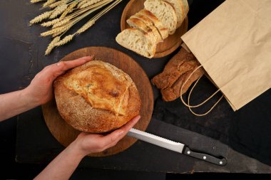 Tam tahıllı ekmek mutfak ahşap tabağına konur ve bıçakla kesilir. Masanın üzerinde taze ekmek var. Mutfak masasında taze ekmek. Sağlıklı beslenme ve geleneksel fırın konsepti. Üst ekran.