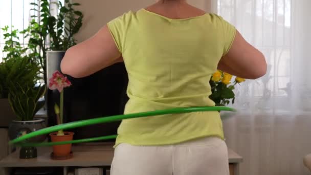 腰の周りにスポーツフープを巻き込む女性 女性は自宅のリビングルームでスポーツをしています — ストック動画