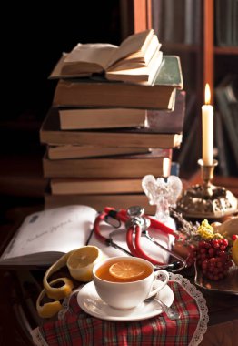 Bir yığın antika kitap, bir fonendoskop, limonlu bir fincan çay, açık bir not defteri, ahşap bir masada tıbbi bitkiler.