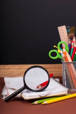 Tahta, kitaplar, kalemler, açılmış boş defterler okul masasında yatıyor.