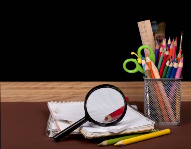 Tahta, kitaplar, kalemler, açılmış boş defterler okul masasında yatıyor.