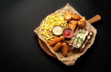 chicken fillet fried in batter with sauce on a wooden board on a black background
