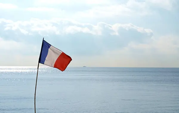 French flag. The French flag flutters against the backdrop of the summer sea and blue cloudless sky. The atmosphere of a picturesque beach
