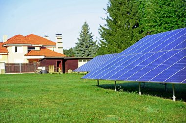 Konut alanındaki yeşil çimlere kurulmuş çevre dostu güneş panelleri yenilenebilir enerjiye ve sürdürülebilir yaşama bağlılığını gösteriyor.