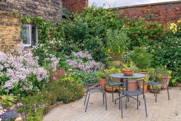 stock image Charming cottage garden with terracotta planters, table and chairs.