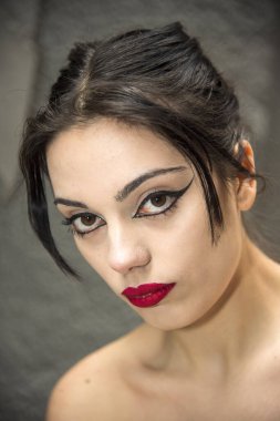 Göz kamaştırıcı makyajlı ve canlı kırmızı rujlu çarpıcı esmer kadın zarif pozlar veriyor, kendine güveni ve cazibesi tam.