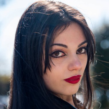 Uzun, koyu renk saçlı, kırmızı rujlu güzel bir kadın arkasını kolluyor.