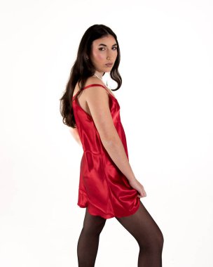 İnci kolyeli kırmızı saten elbisesini sergileyen genç bir kadın bir moda çekiminde beyaz bir arkaplanda poz veriyor.