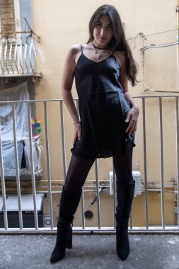 Şık, siyah bir elbise, tayt ve çizme giymiş, şık ve şehirli bir görünüm yaratıyor.