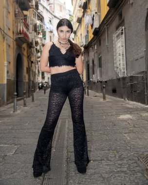 Siyah dantel kıyafetli genç bir kadın, Avrupa 'nın dar bir sokağında, tarihi mimariye karşı modern moda sergiliyor.