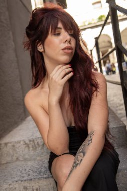 Kentsel basamaklarda oturan kızıl saçlı manken, çağdaş stil ve şehir ortamında ilham verici zarafet sergiliyor.