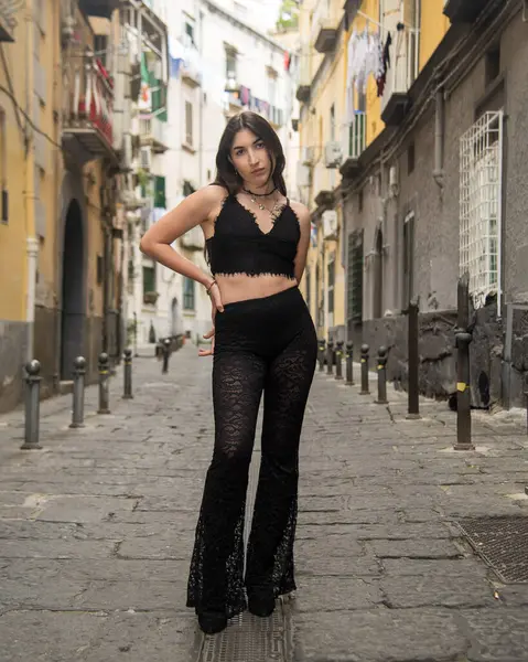 Napoli sokaklarında poz veren uzun kahverengi saçlı genç bir kadın siyah bluz ve dantel pantolon giyiyor.