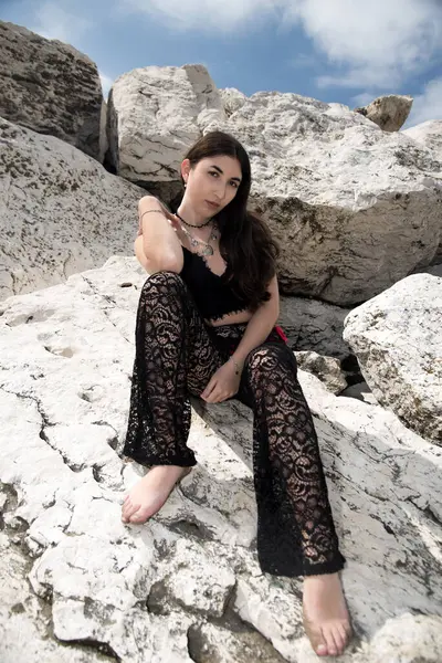 Dantel kıyafetli genç bir kadın beyaz kayalık arazide oturuyor, güneşli bir günün tadını çıkarıyor parlak mavi gökyüzünün altında sakin bir ifadeyle.
