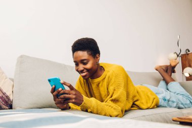 African woman using cellphone at home sitting on the sofa