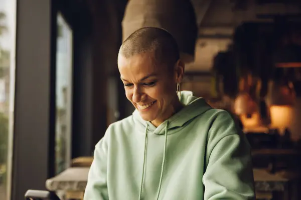 Bald woman smiling using a device indoor. High quality photo
