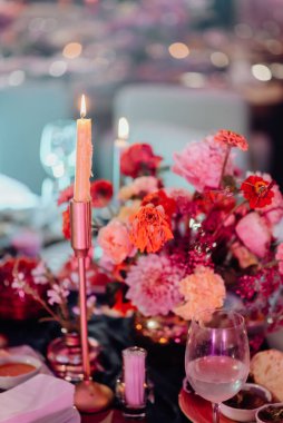 İki kişilik romantik bir akşam. Çatal bıçakla servis edilen ve üzerinde yanan mumlar bulunan taze çiçeklerle süslenmiş bir festival masası..