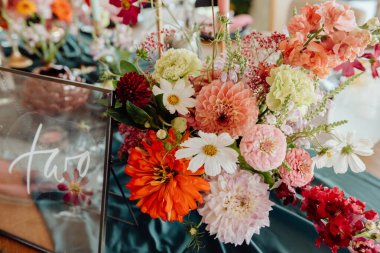 Detail of a table setting in a restaurant. Fresh flowers in a vase of red, white and orange with green sprigs on a dark green tablecloth