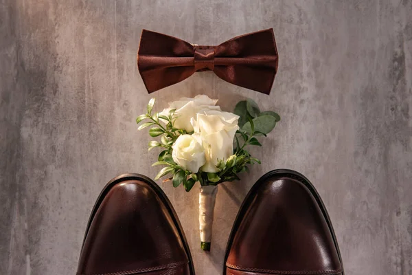 在新郎的巧克力色蝴蝶旁边 靠近棕色皮鞋的袜子 有一小束玫瑰 上面有绿色的小枝条 上面放着一枝杜邦尼 放在一张阁楼桌子上 — 图库照片