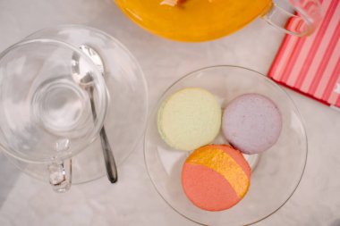 Kafede beyaz bir masa, üzerinde cam bir tabak ve kaşıklı bir fincan var. Bir tabakta üç badem kurabiyesi var. Yakınlarda bir vazo portakal suyu var. Masanın üzerinde bir defter var.