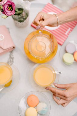 Cafe misafirleri masaya oturur ve cam bardaklara portakal suyu dökerler. Yukarıdan bak. Masanın üzerinde tabaklar halinde badem kurabiyeleri var. Bir vazo suyun içinde bir gül var. Yaz günü