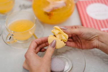 Kız elleriyle badem kurabiyesi kırıyor. Arka planda sarı çaydanlık ve çay bardağı var..