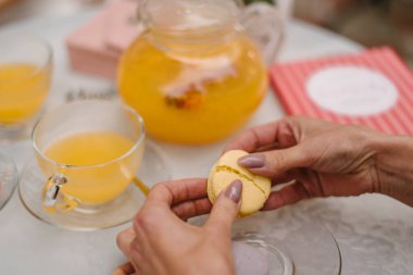 Kız elleriyle badem kurabiyesi kırıyor. Arka planda sarı çaydanlık ve çay bardağı var..