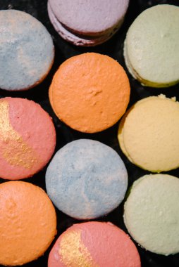 Tatlılar, siyah bir masanın üstünde renkli Fransız kurabiyeleri.