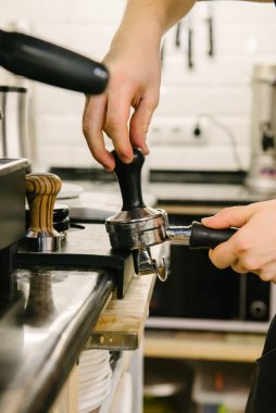 Bir kafede bir barista kahve tutacağına kahve basar ve kahve demlemeye hazırlanır..