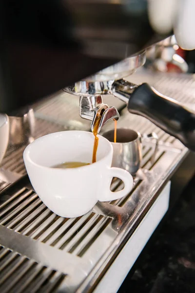 stock image In the white cup that is in the coffee machine, fresh coffee with foam flows out of the holder