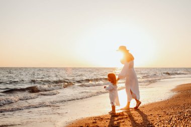 Genç bir anne küçük kızını elinden tutar ve birlikte okyanus boyunca gün batımına doğru yürürler. Beyaz elbiseli ve uzun saçlı kızlar rüzgarı geliştiriyor.