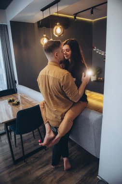 Bir kız, bir erkeğin karşısındaki kanepede oturuyor. Adam nazikçe kızın belini tuttu. Kız, adamın yüzüne elleriyle dokunuyor. Bulanık siyah arkaplan.