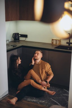 Genç bir çift mutfakta yerde oturuyorlar. Kız, gülümsüyordu, bacaklarını adamın üzerine attı ve adamın yanağına eliyle hafifçe dokundu. Adam gözlerini kapattı ve kızı bacağından tuttu..