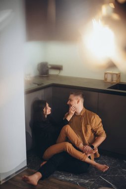 Genç bir çift mutfakta yerde oturuyorlar. Kız, gülümsüyordu, bacaklarını adamın üzerine attı ve adamın yanağına eliyle hafifçe dokundu. Adam gözlerini kapattı ve kızı bacağından tuttu..