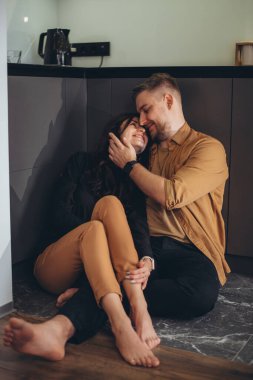 Genç bir çift mutfakta yalınayak oturuyor. Kız, gülümseyerek, bacaklarını adamın üzerine attı ve kendini onun gözlerine bastırdı. Bir erkek bir kızın yüzüne eliyle dokunur.