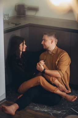 Genç bir çift mutfakta yerde oturuyorlar. Kız, gülümsüyordu, bacaklarını adamın üzerine attı ve gözlerinin içine baktı. Adam kıza bakıyor, gülümsüyor ve elini tutuyor..