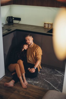 Genç bir çift mutfakta yalınayak oturuyor. Kız bacaklarını adamın üzerine attı ve onun omzuna yattı. Kızın elini tutan adam.