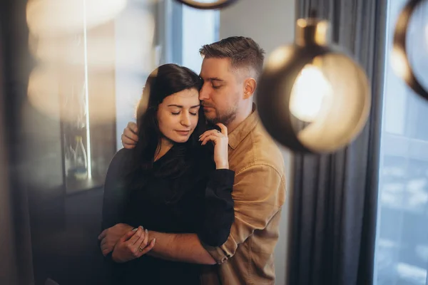 A married couple is hugging in the kitchen at home. The girl stands with her back to the guy and touches the guys beard with her hand. A man hugs and presses his cheek to a girl