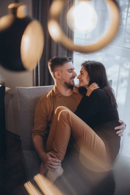 Kız, erkeğin kollarına sarılmış oturuyor. Adam nazikçe kızı tutuyor ve gözlerinin içine bakıp gülümsüyor. Birbirine aşık bir çift. Ön planda bulanıklık. Parılda