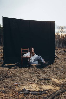 Güzel üzgün bir kız, kara bir arka planda, ormansızlaşmanın ortasında yerde oturuyor. Her yerde ağaç kütükleri var. Ormansız bir orman. Doğayı yok etti. Üzgün kız.