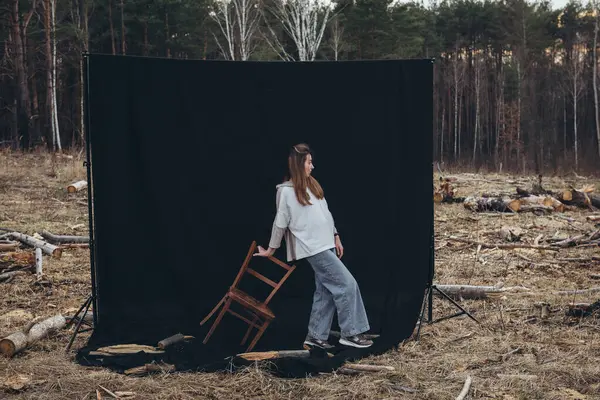 Güzel üzgün bir kız, kara bir arka planda, ormansızlaşmanın ortasında yerde duruyor. Her yerde ağaç kütükleri var. Ormansız bir orman. Doğayı yok etti. Üzgün kız.