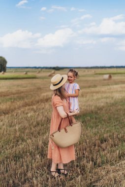 Uzun elbiseli ve hasır şapkalı genç bir anne küçük kızını elinden tutar. Her ikisi de hasat edilen buğday tarlasında yürür. Bir saman balyasının arka planında