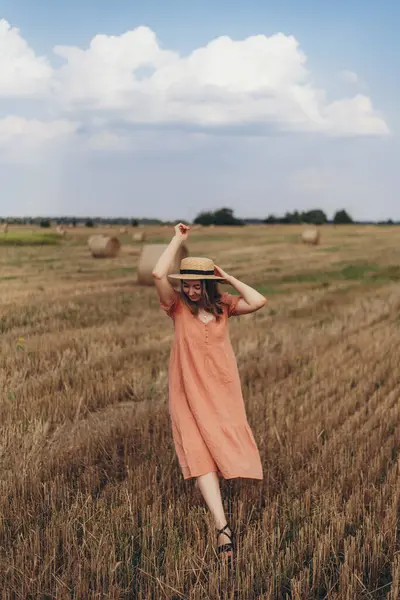 Uzun elbiseli ve uzun saçlı güzel bir kız biçilmiş buğday tarlasında yürüyor. Mavi gökyüzü ve bulutların arka planında