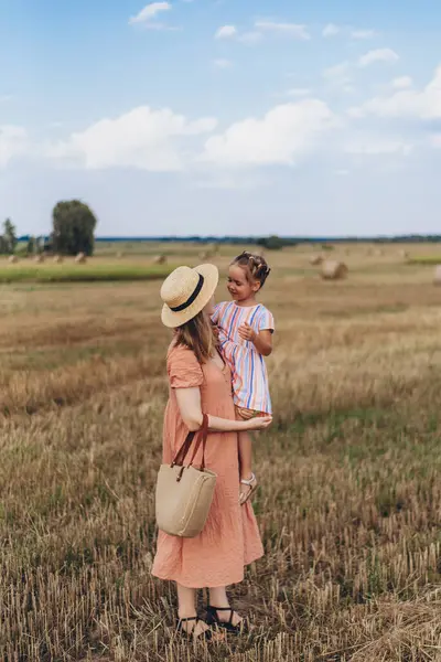드레스와 모자를 어머니는 손으로 이끈다 수확된 밀밭을 가로질러 걸어갑니다 베일의 스톡 사진