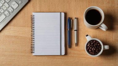 Ofis masası. Laptop, not defteri, kahve, ofis malzemeleri ve beyaz ahşap masadaki yeşil yapraklarla estetik çalışma alanı. Merkez ofis, asgari bohem tarzı, üst görünüm.